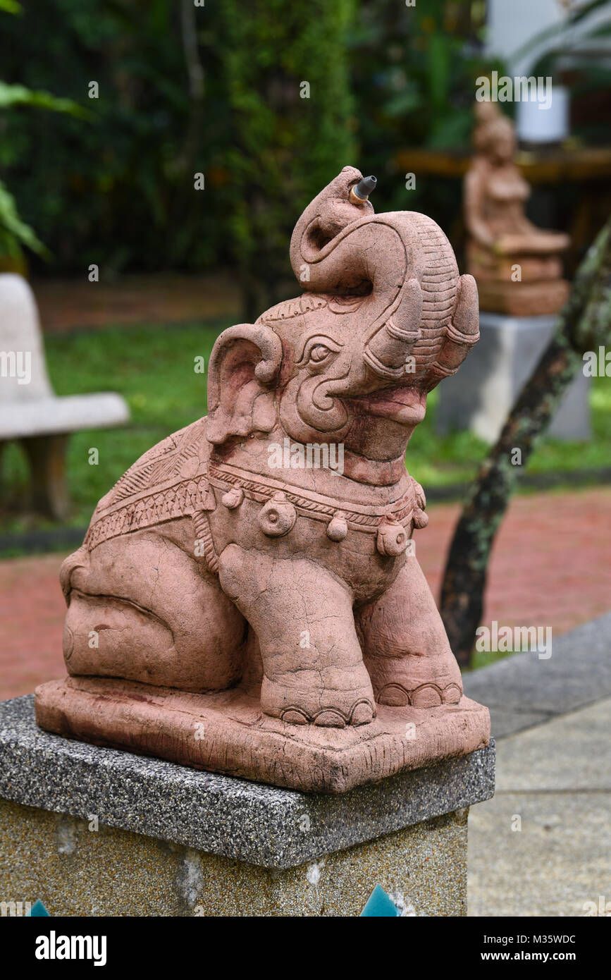 Stein Skulptur Statue eines Elefanten sitzend mit seinem Stamm bis fröhlich und lachend in einem Garten in Thailand bei Tageslicht Stockfoto