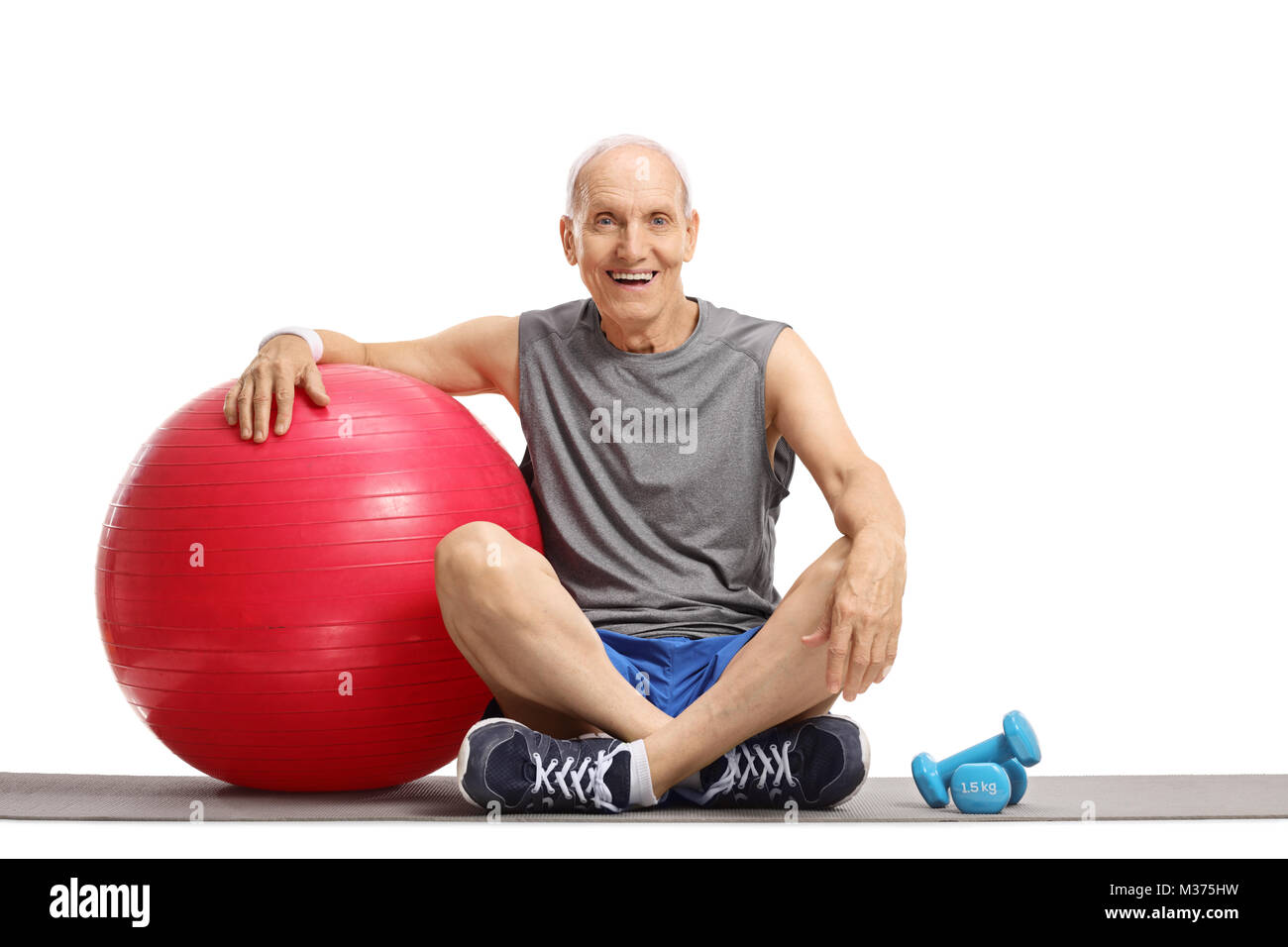 Älterer Mann mit einem Pilates Ball und Kurzhanteln auf einer Gymnastikmatte auf weißem Hintergrund Stockfoto