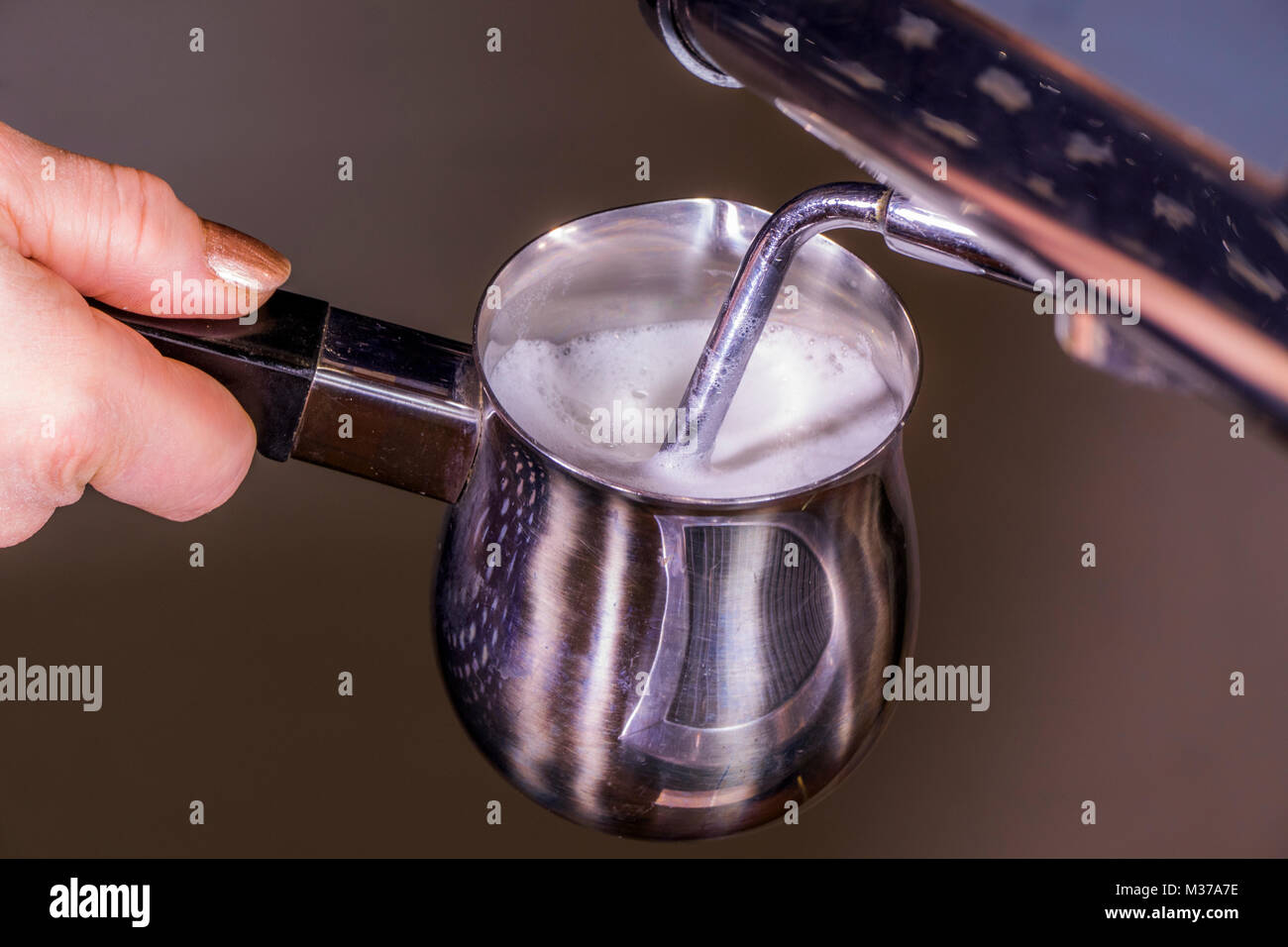 Woman's Hand mit einem Edelstahl milchaufschäumung Krug, unter Dampf-/Dämpfen Zauberstab der eine gewerbliche Espressomaschine, Schaum zu erzeugen. UK. Stockfoto