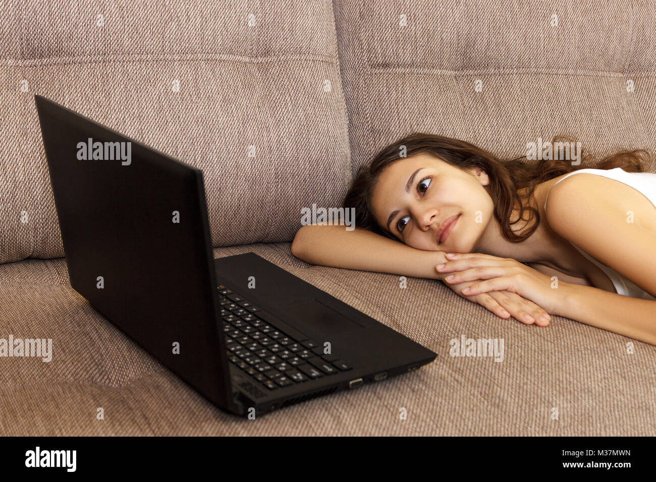 Einzelne Mädchen Suche online Inhalte in einem Laptop auf einer Couch im Wohnzimmer zu Hause liegen. Stockfoto