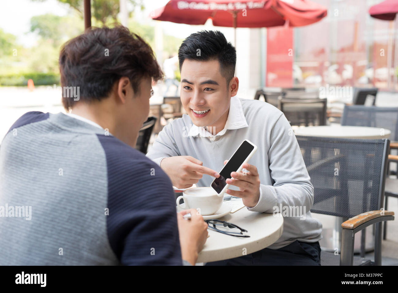 Asiatische junge Männer genießen gerade auf Mobiltelefon zusammen in ein Café mit Kaffee auf den Tisch. Stockfoto