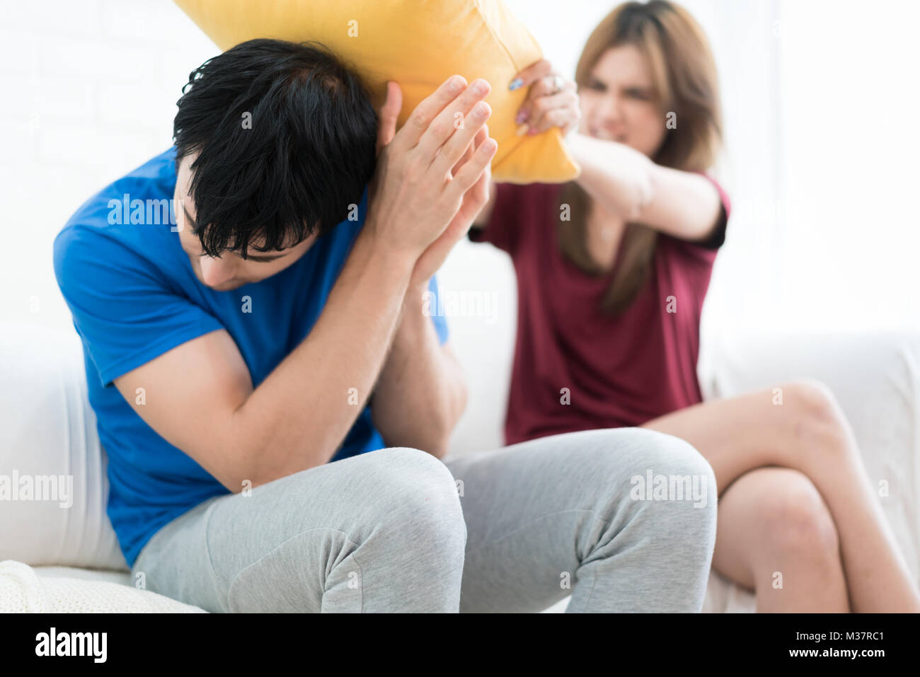 Junges Paar Streit ling emotional zu Hause, Frau mit einem Kissen angreift, man ist verwirrt, argumentieren auf Familie Haushalt. Probleme in der Familie Konzept Stockfoto