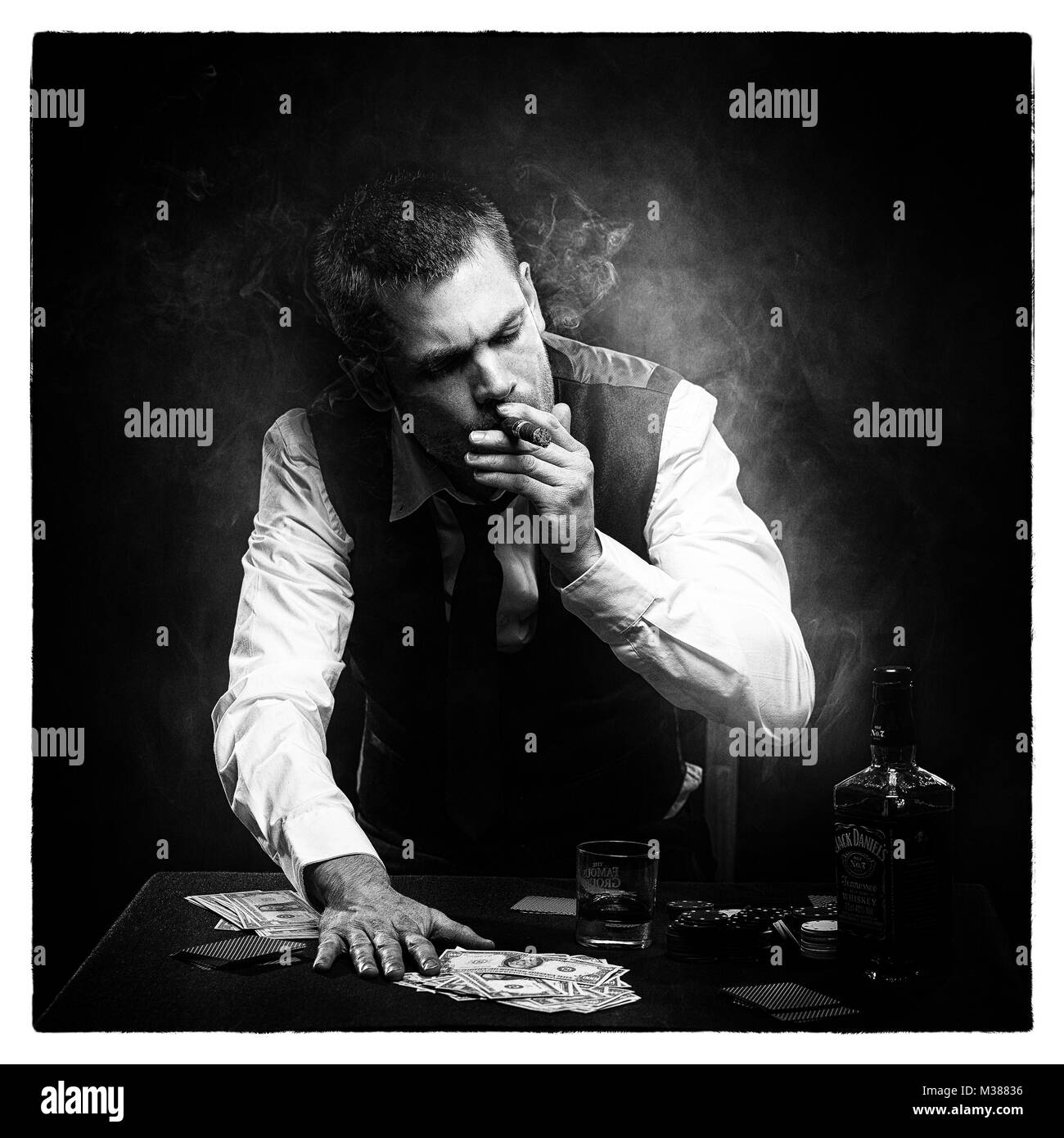 Harter Gangster, der eine Zigarre raucht und Whisky am Pokertisch trinkt Stockfoto