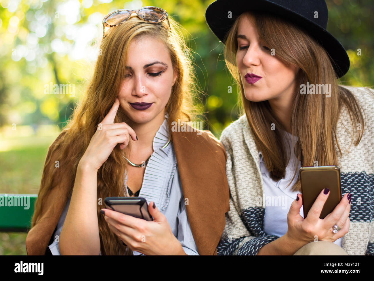Weibliche Freunde auf der Suche nach Smart Phone auf einer Parkbank Stockfoto