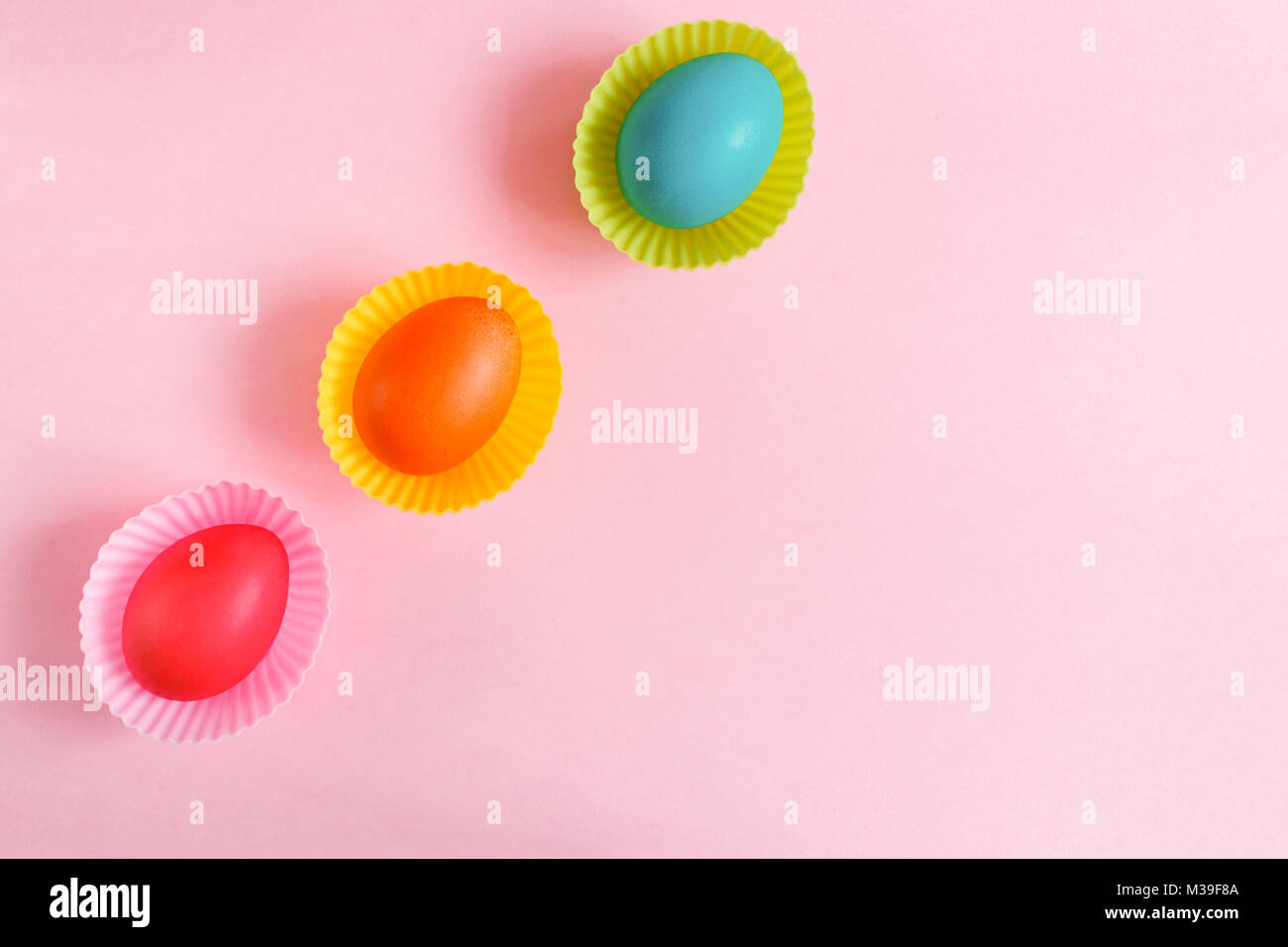 Ostern Hintergrund. Flach drei bunt bemalte Eier in Rosa geschnitzte cupcakes Formen sind diadonally liegen auf einem rosa Hintergrund mit kopieren. Stockfoto