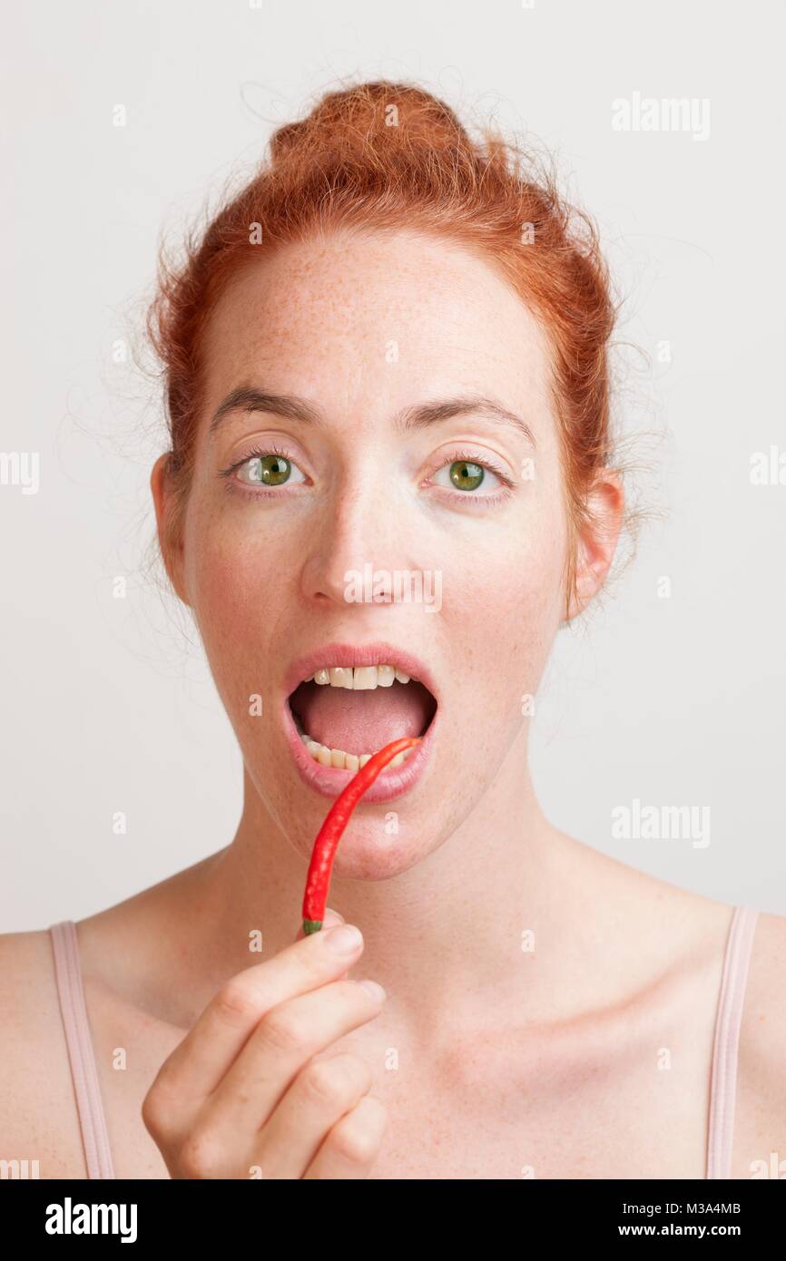 MODEL RELEASED. Frau mit roten Chili vor Ihrem offenen Mund. Stockfoto