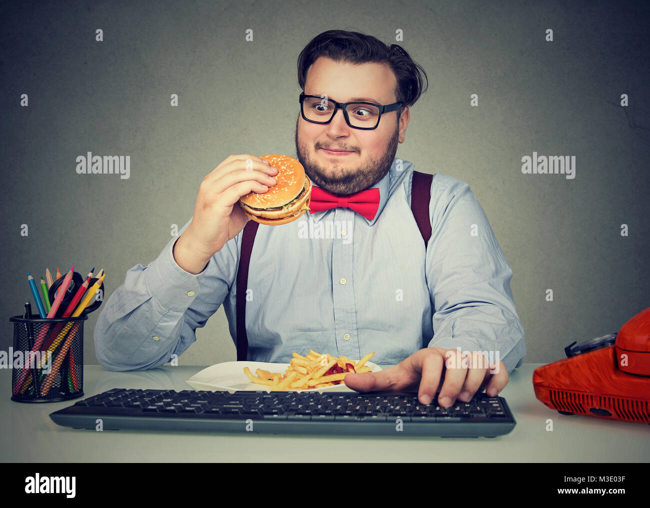Beleibten Mann in Gläser Essen fast food beim Arbeiten im Büro und zu überessen. Stockfoto