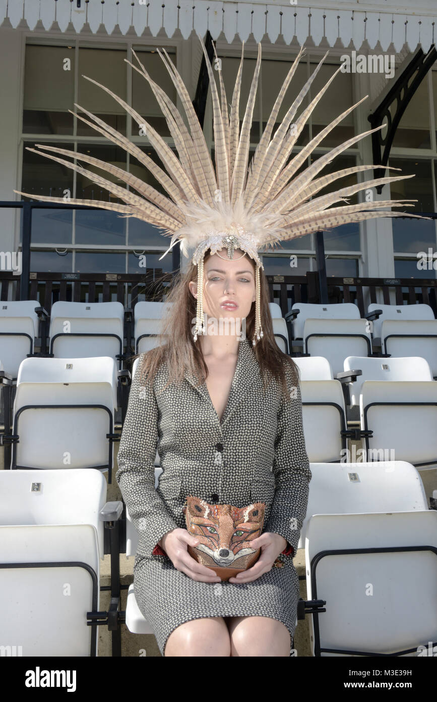 Schöne Mädchen mit einem spektakulären Kopf Kleid und ein Maßanzug sitzt in den Ständen zu einem Cricket Ground - sie hat ein Fuchs Handtasche Stockfoto