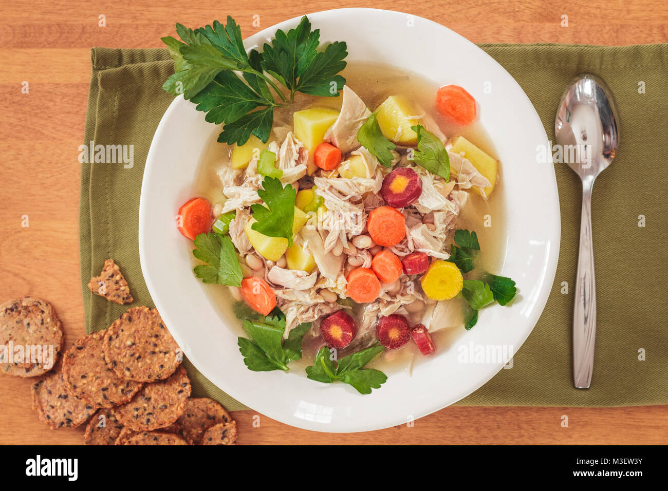 Ansicht von oben mit hausgemachten Huhn und weißen Bohnen Suppe in einer weißen Schüssel. Vollkorn cracker Akzent die Einstellung mit grünen Serviette und Löffel. Stockfoto