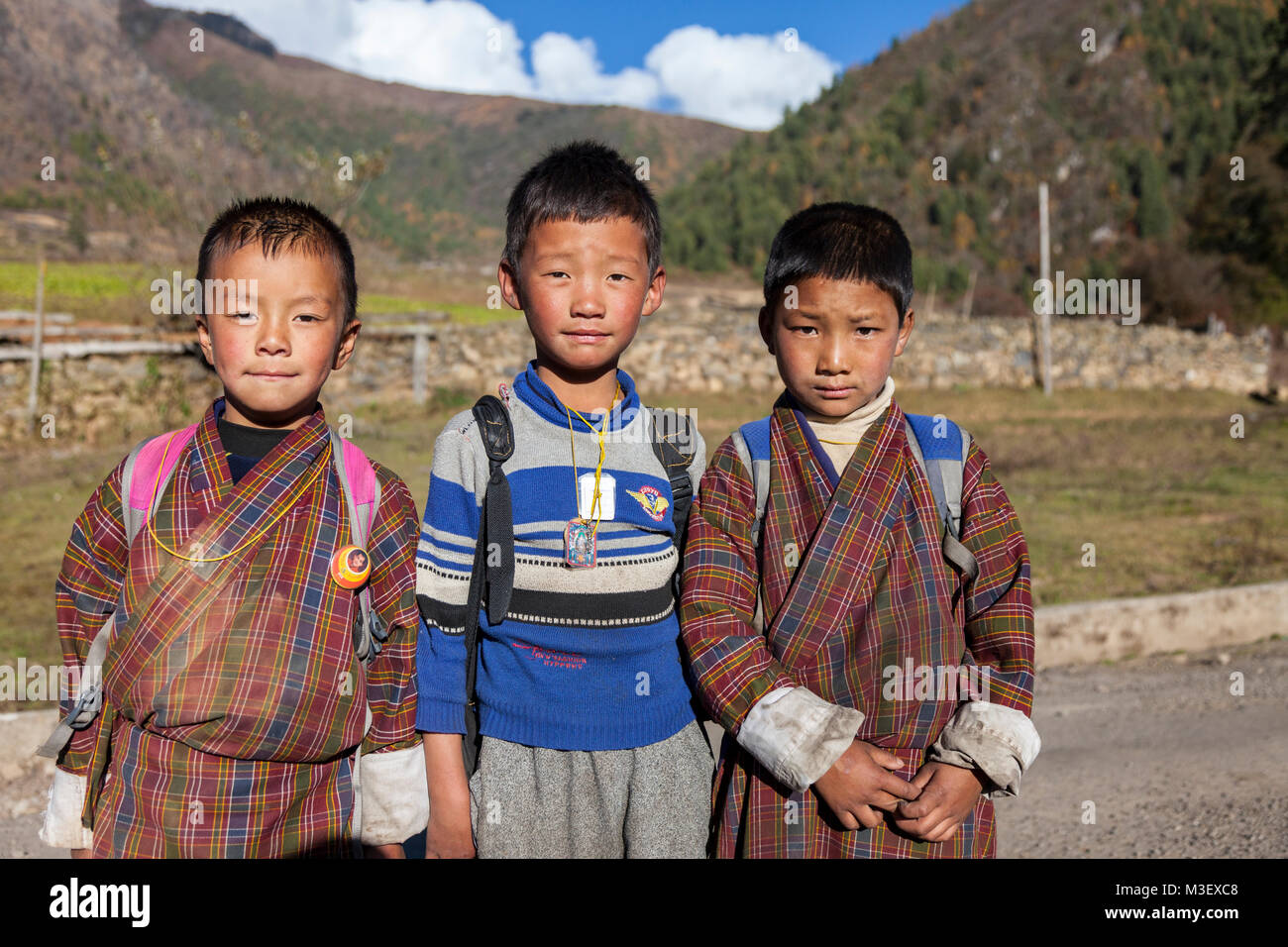 Phobjikha, Bhutan. Kikorthang Dorf. Drei Schuljungen, zwei tragen traditionelle Gho, einer in westliche Kleidung. Stockfoto