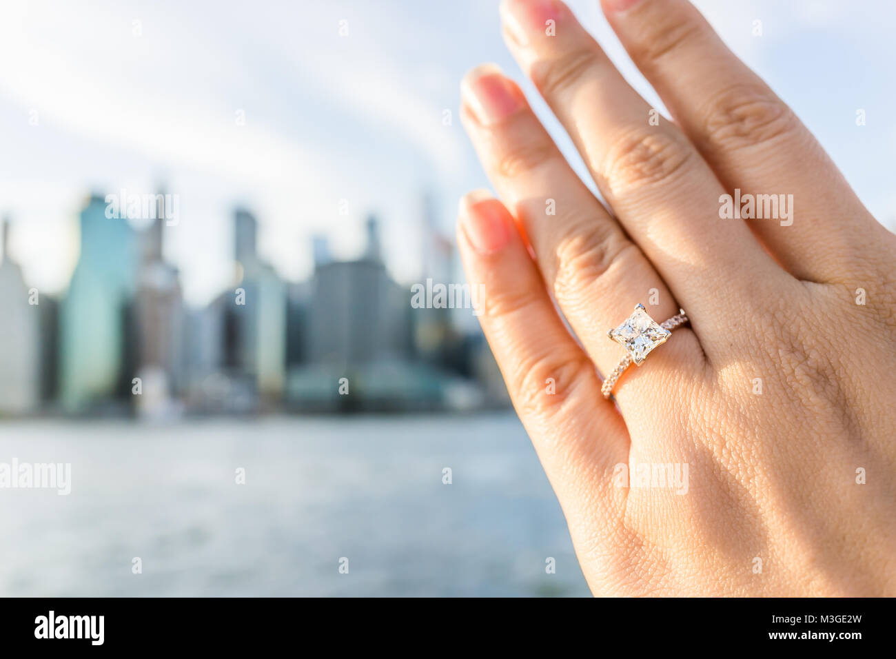 Die junge Frau mit Diamond Engagement Ring princess Cut, Gold draußen im Freien in NYC New York City Brooklyn Bridge Park am East River, Stadtbild Stockfoto