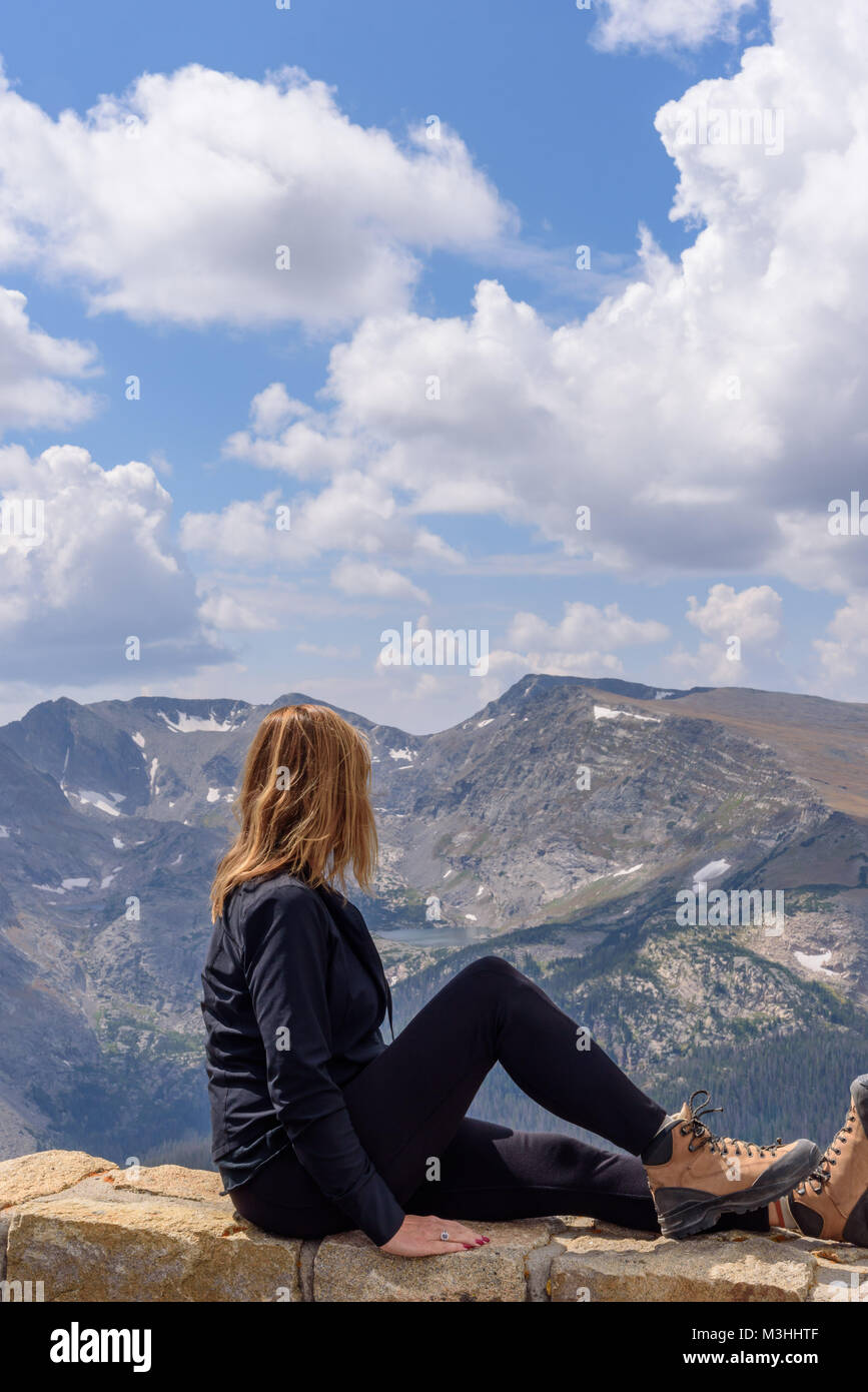 Junge Frau sitzt auf der Steinmauer am Aussichtspunkt im Rocky Mountain National Park Stockfoto