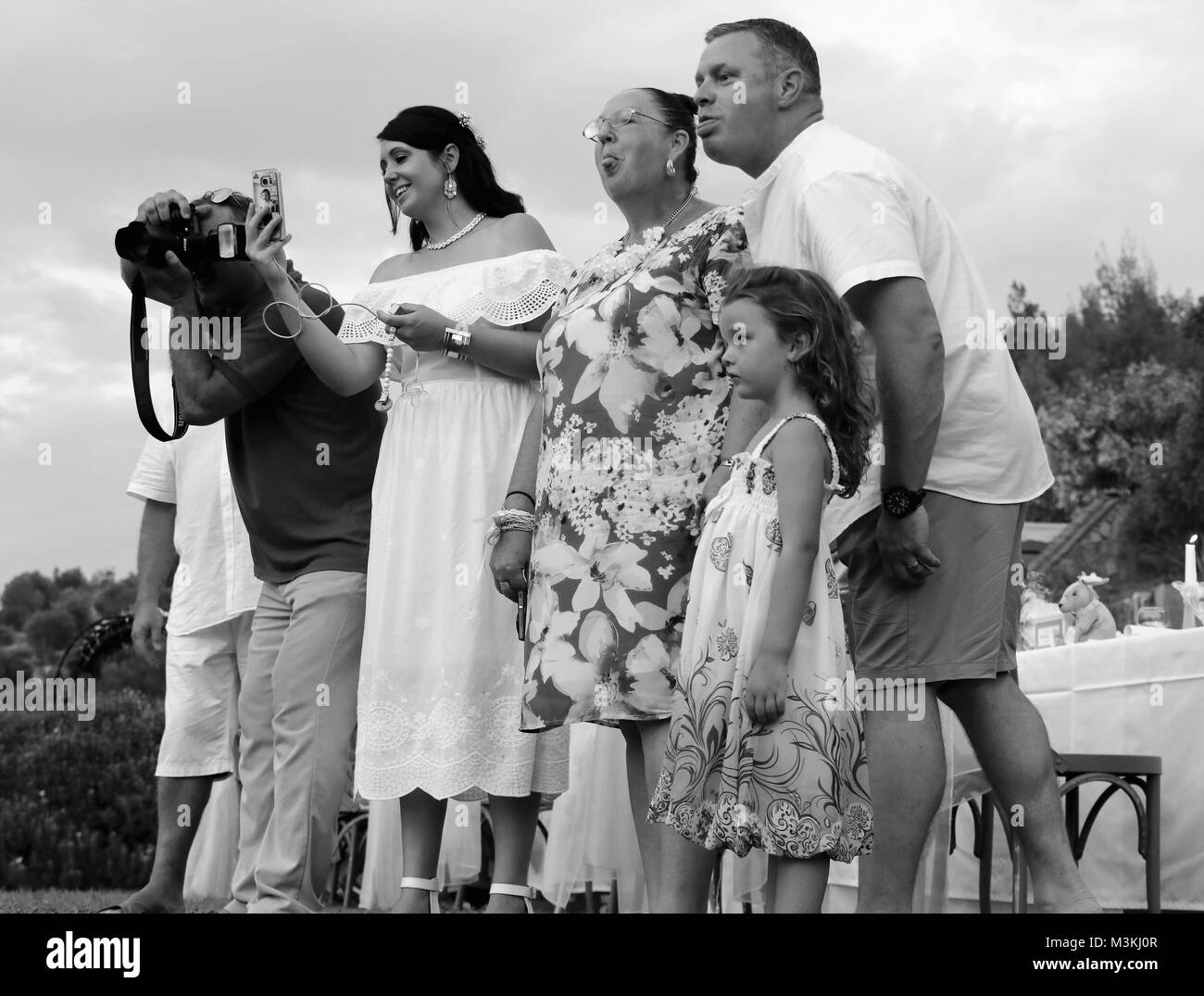 Eltern und Großmutter macht's Gesicht, um zu versuchen, das Kind zu lachen oder lächeln, während Sie bei einer Hochzeit in Fethiye, Türkei, 4. August 2017 Stockfoto
