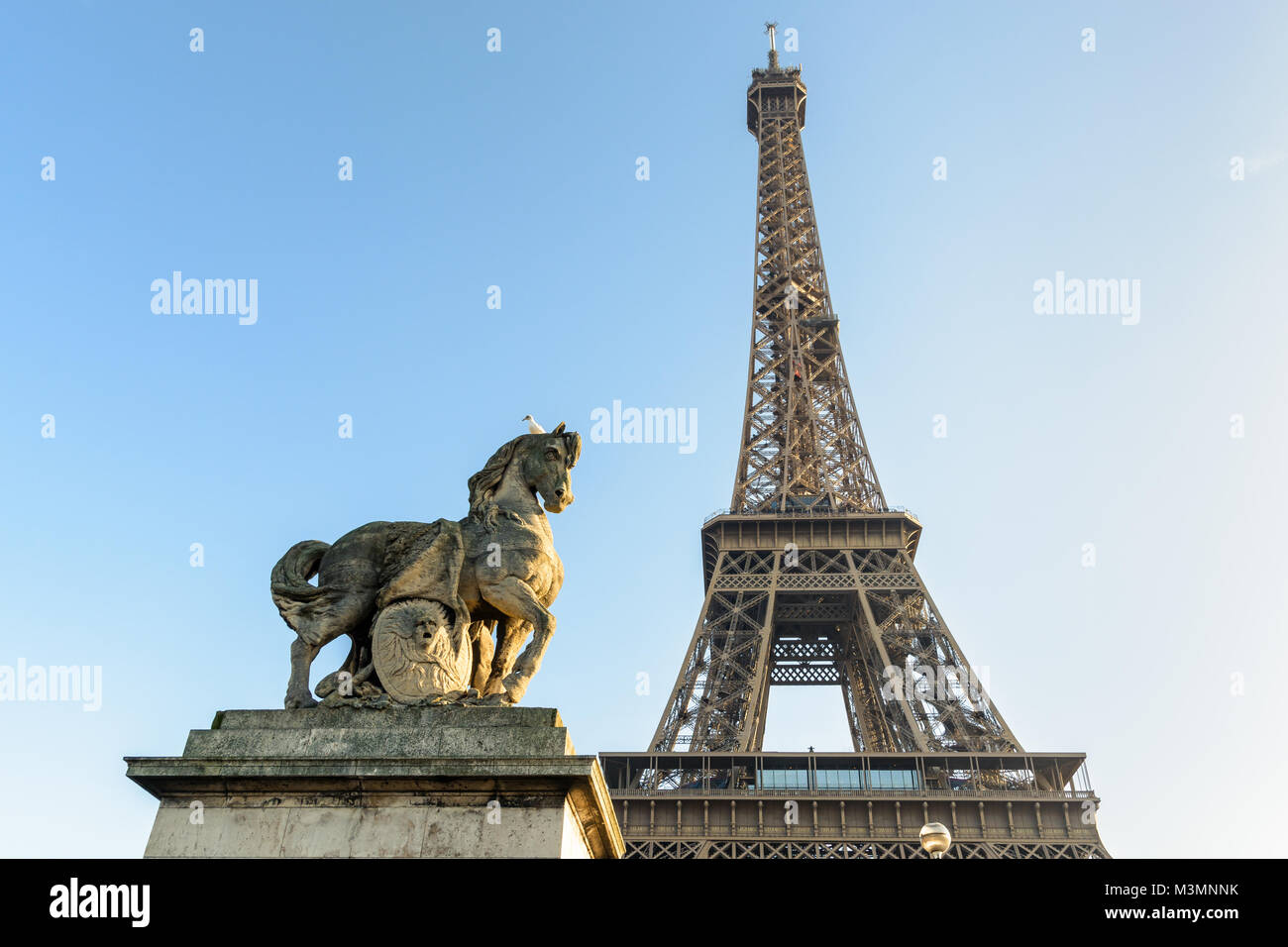 Low Angle Blick auf den Eiffelturm in Paris, von der Iena Brücke gegen den blauen Himmel gesehen, mit einem Equestrian Stein Statue im Vordergrund. Stockfoto