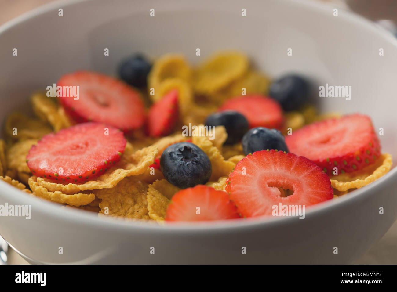 Corn Flakes mit Beeren in Weiß Schüssel für das Frühstück auf dem Tisch Stockfoto