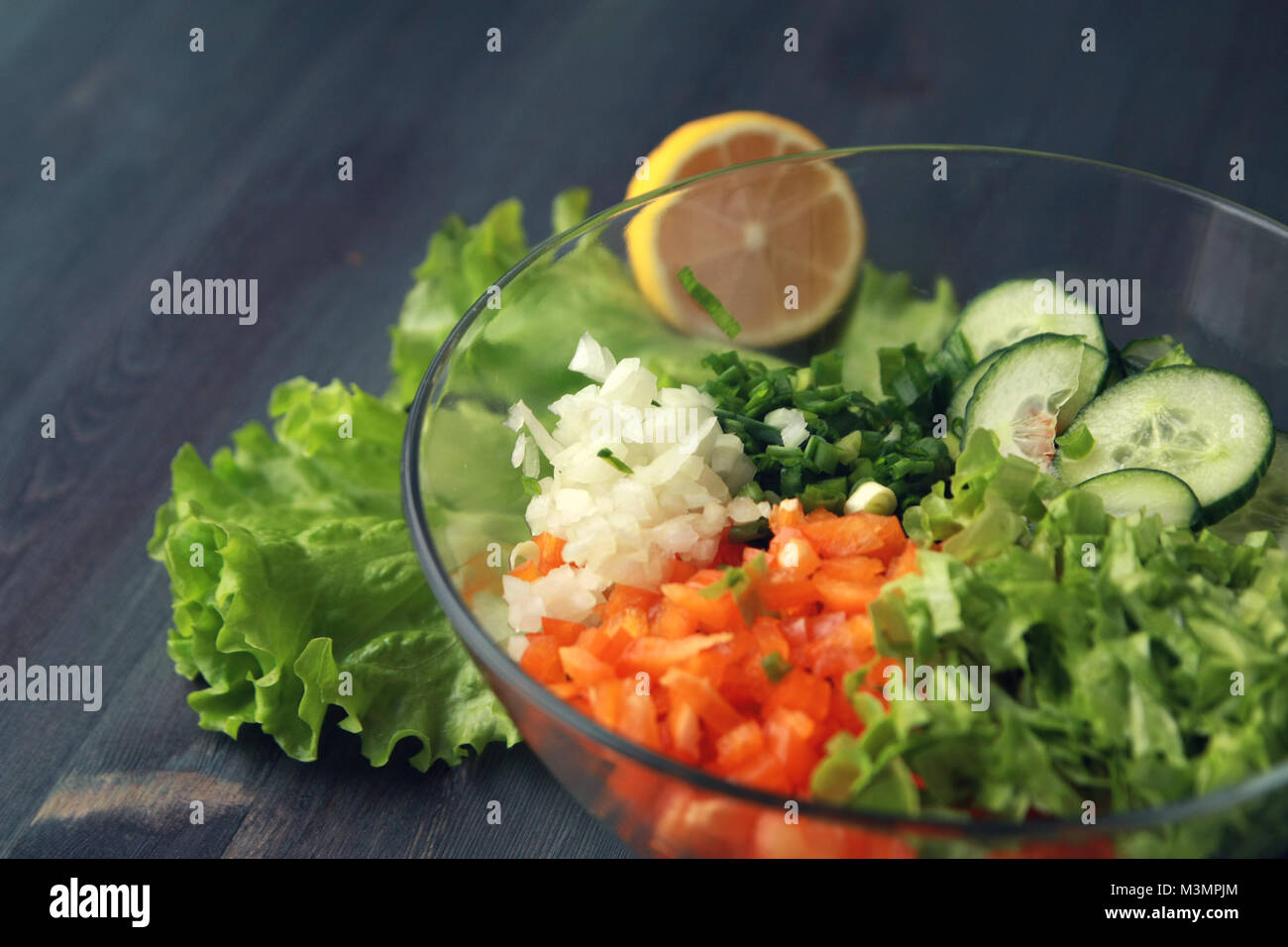 Glasschale mit geschnittenen Gemüse für einen Salat. Close Up. Paprika, Zwiebeln, Blattgemüse und Tomaten in Stücke geschnitten. Holz- Hintergrund. Stockfoto