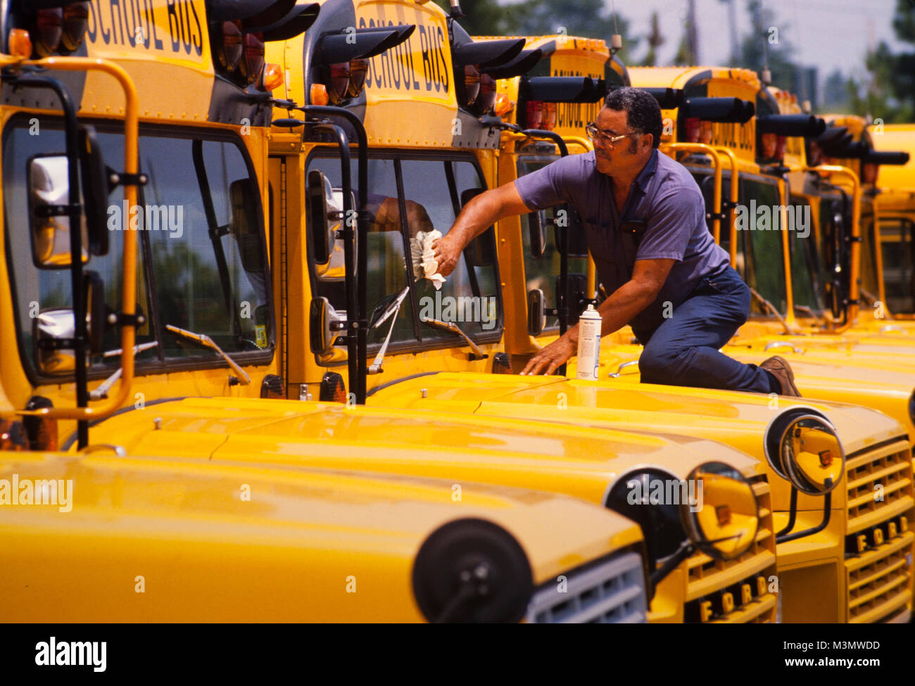 Ein Wartung Arbeiter reinigt die Windschutzscheiben der Schulbusse an einer Schule garage Stockfoto
