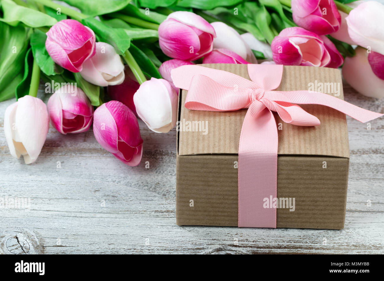 Nahaufnahme einer braunen Geschenkkarton mit rosa Tulpen im Hintergrund auf weißen verwitterte Holzbretter Stockfoto