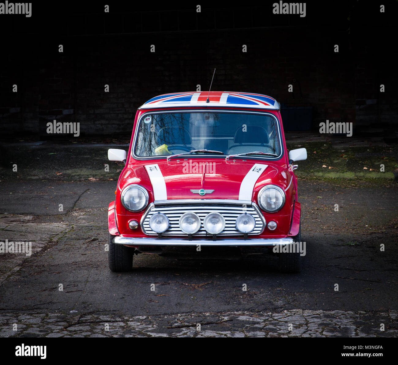 Eine Vorderansicht eines klassischen, rot Mini Cooper mit einem Union Jack  Flagge auf dem Dach und einen großen, chrom Scheinwerfer auf einem dunklen  Hintergrund Stockfotografie - Alamy