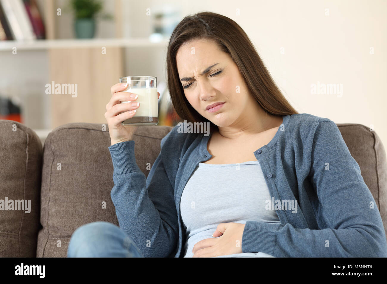 Frau mit Laktoseintoleranz auf einer Couch im Wohnzimmer zu Hause sitzen Stockfoto