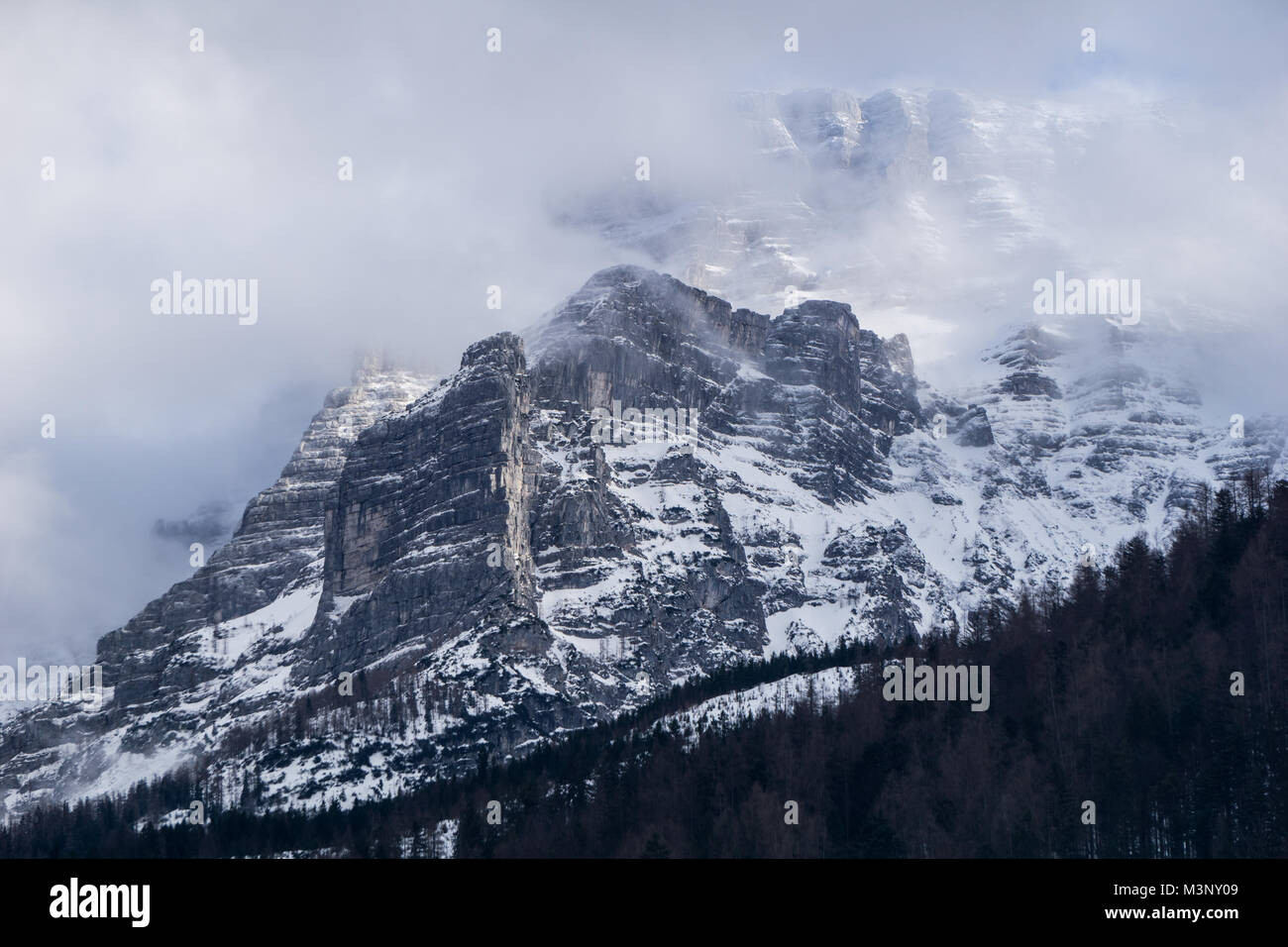 Unglaubliche Berg Szene mit majestätischen Klippen und Cloud ummantelten Gipfeln. Einen kalten, dunklen Wald erstreckt sich auf den Hang unterhalb Stockfoto