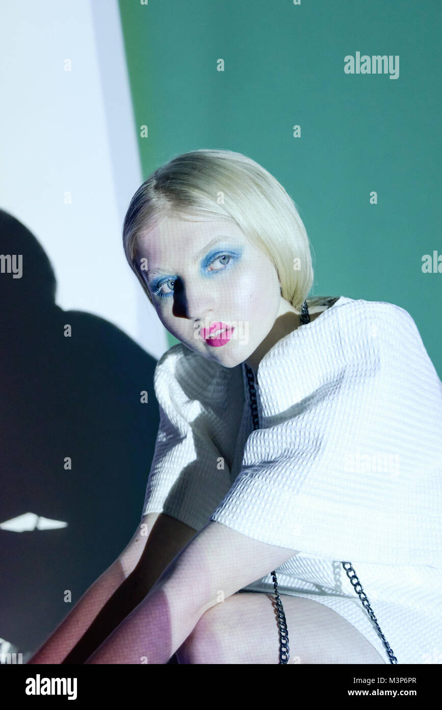 Ein schönes Mädchen mit hellen Stellen und lange blonde Haare hat Licht und Muster auf ihr in einem Studio projiziert - sie trägt einfache Kleidung Stockfoto