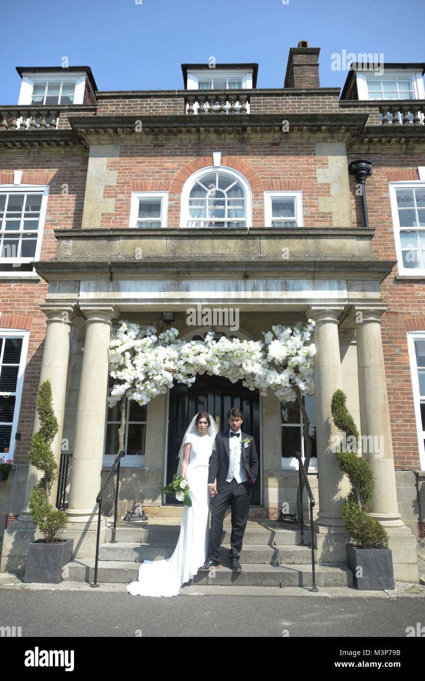 Eine schöne dunkelhaarige Paar am Tag ihrer Hochzeit stellen gemeinsam vor einem englischen Herrenhaus an einem sonnigen Tag Stockfoto