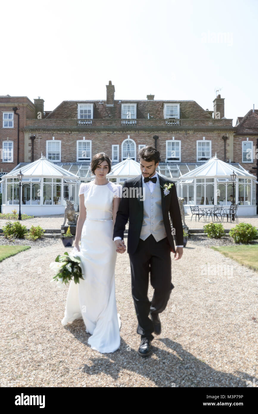 Eine schöne dunkelhaarige Paar am Tag ihrer Hochzeit stellen gemeinsam vor einem englischen Herrenhaus an einem sonnigen Tag Stockfoto