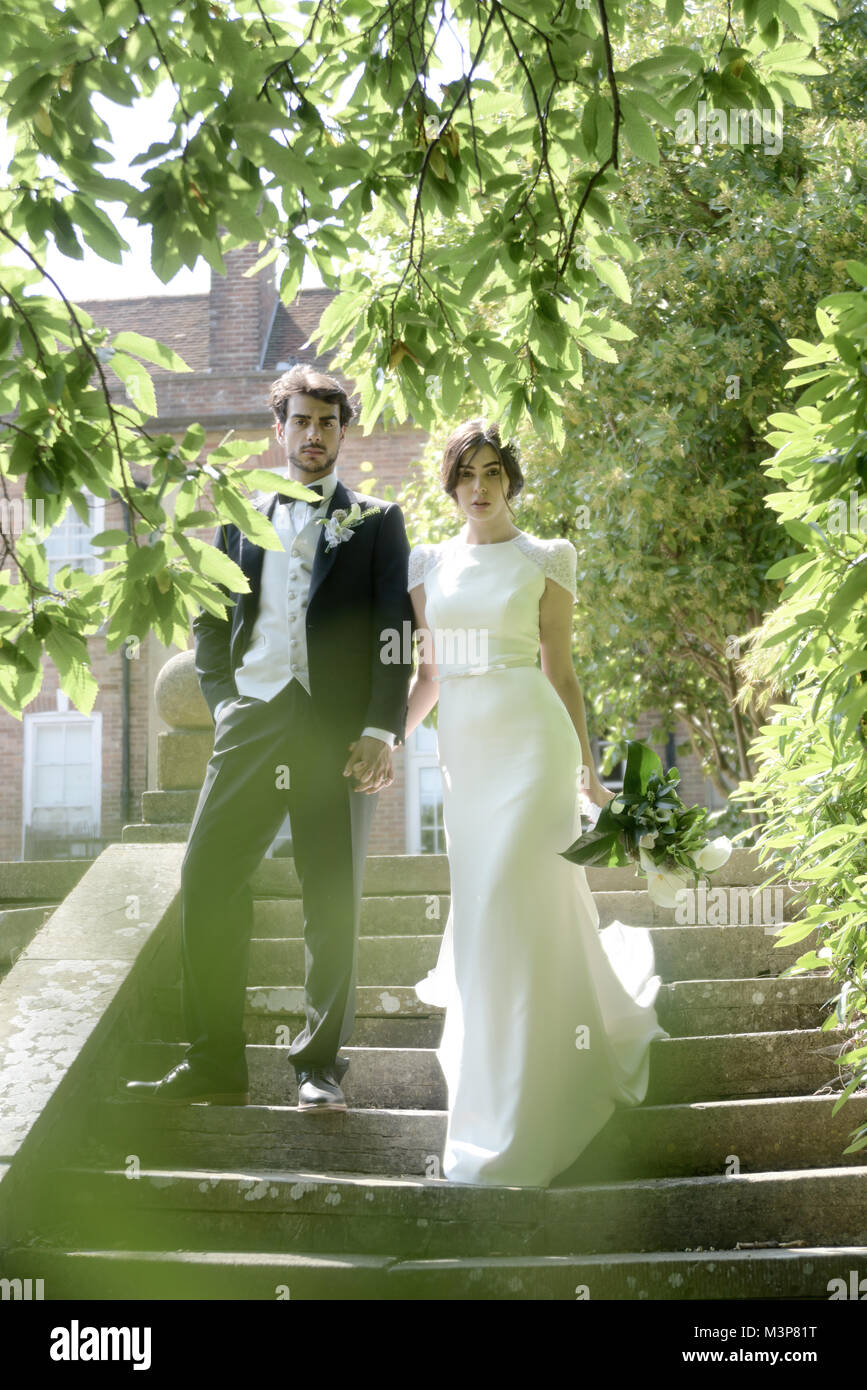 Schöne dunkelhaarige Braut und Bräutigam auf eine gestaltete Hochzeitstag - traditionelles weißes Kleid/schwarzen Anzug - Art déco-Stil mit hellen, sonnigen Tag Stockfoto