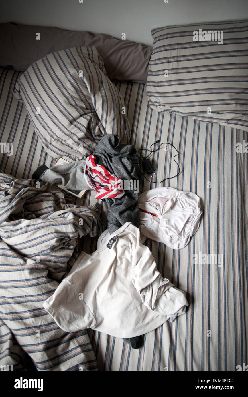 Luftaufnahme eines männlichen Jugendlichen ungemachten Bett mit verstreuten Kleider und -ladegerät Stockfoto
