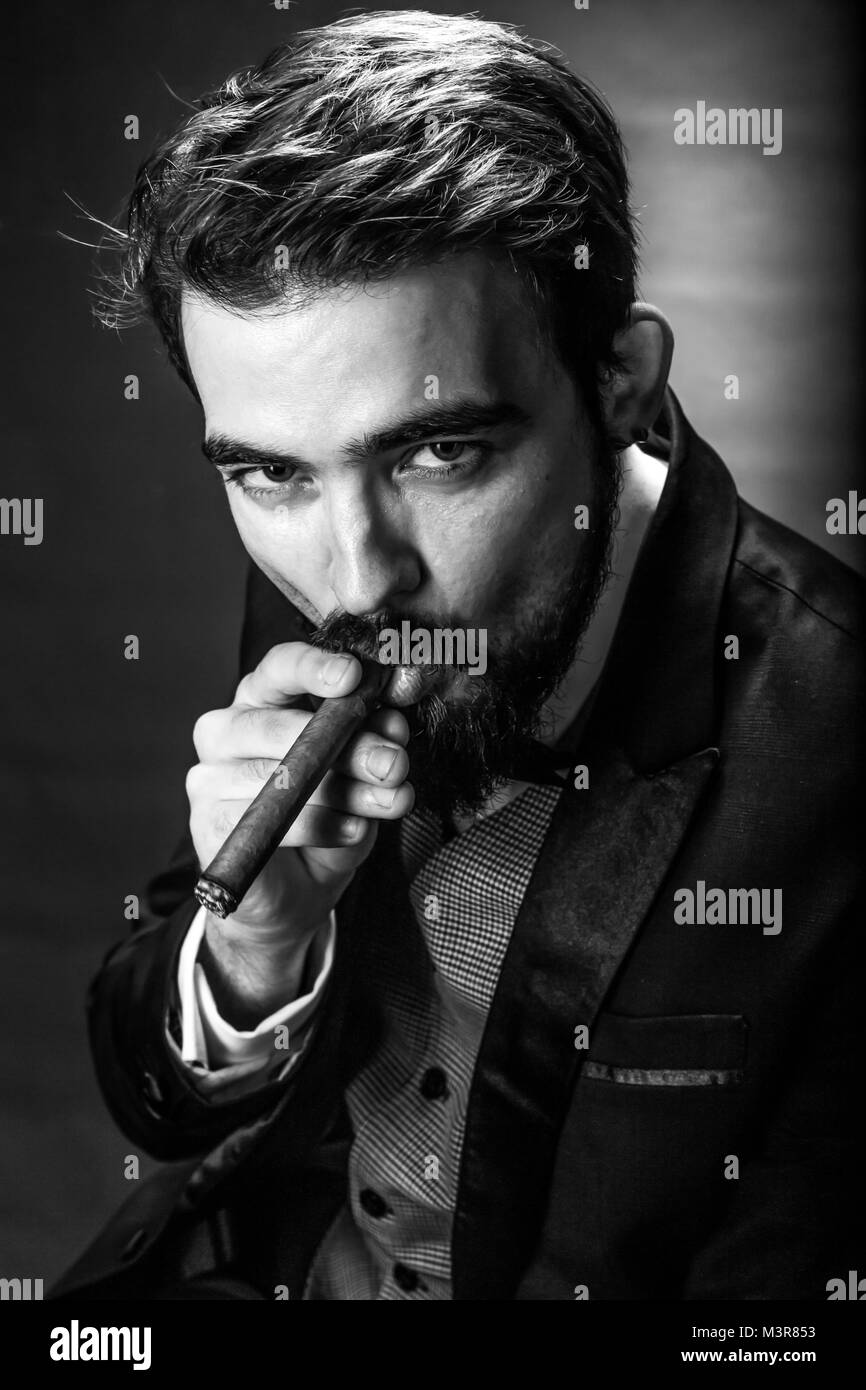Schwarz-weiß-Porträt von bärtigen rauchen Zigarre Gentleman in einem Anzug perzeptiven auf den Betrachter auf der Suche Stockfoto