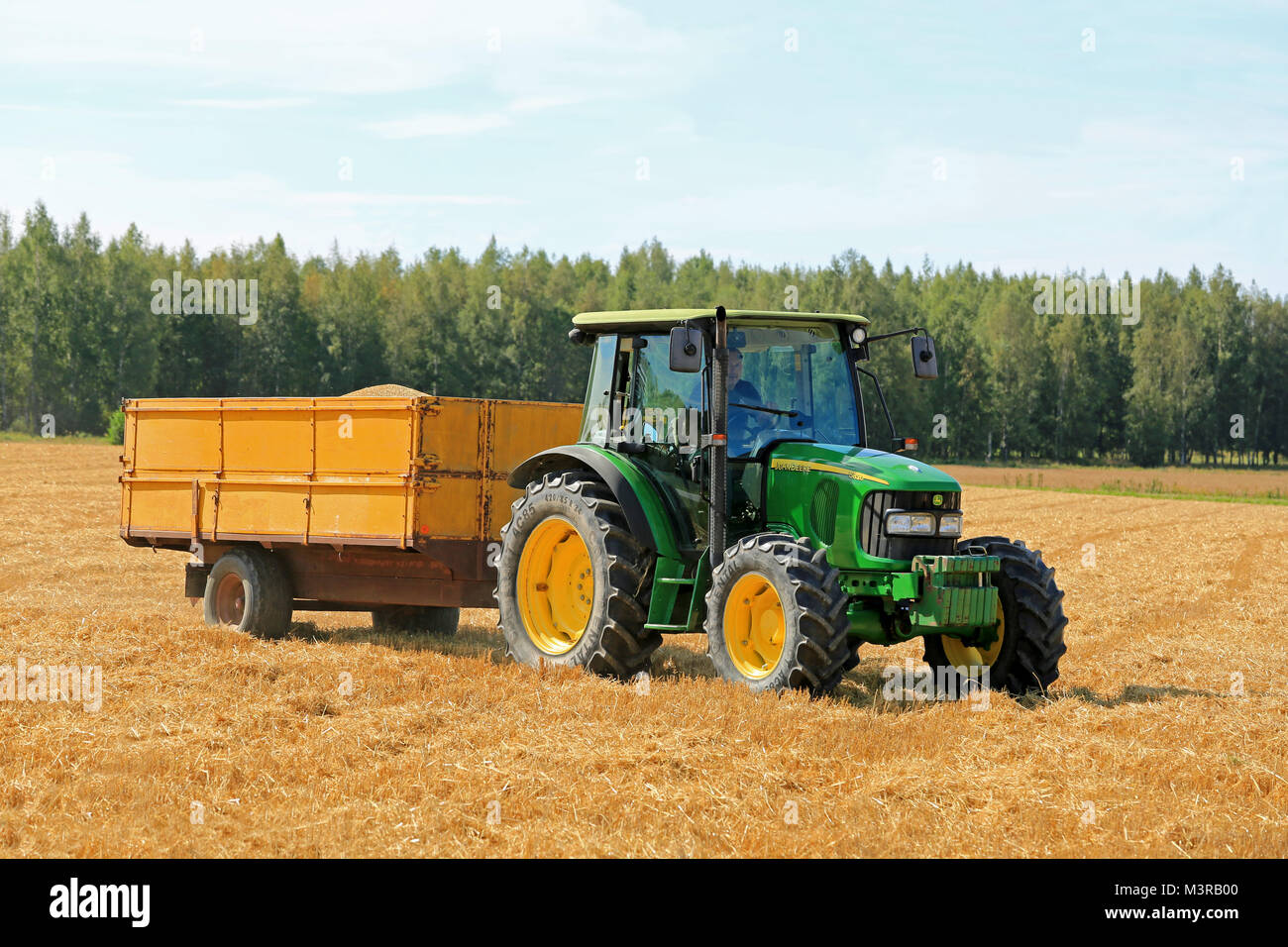 RAASEPORI, Finnland - 17. AUGUST 2014: Nicht identifizierte Bauer fahren eines John Deere 5820 Traktoren und Anhänger voller Körner. John Deere 5820 wa Stockfoto