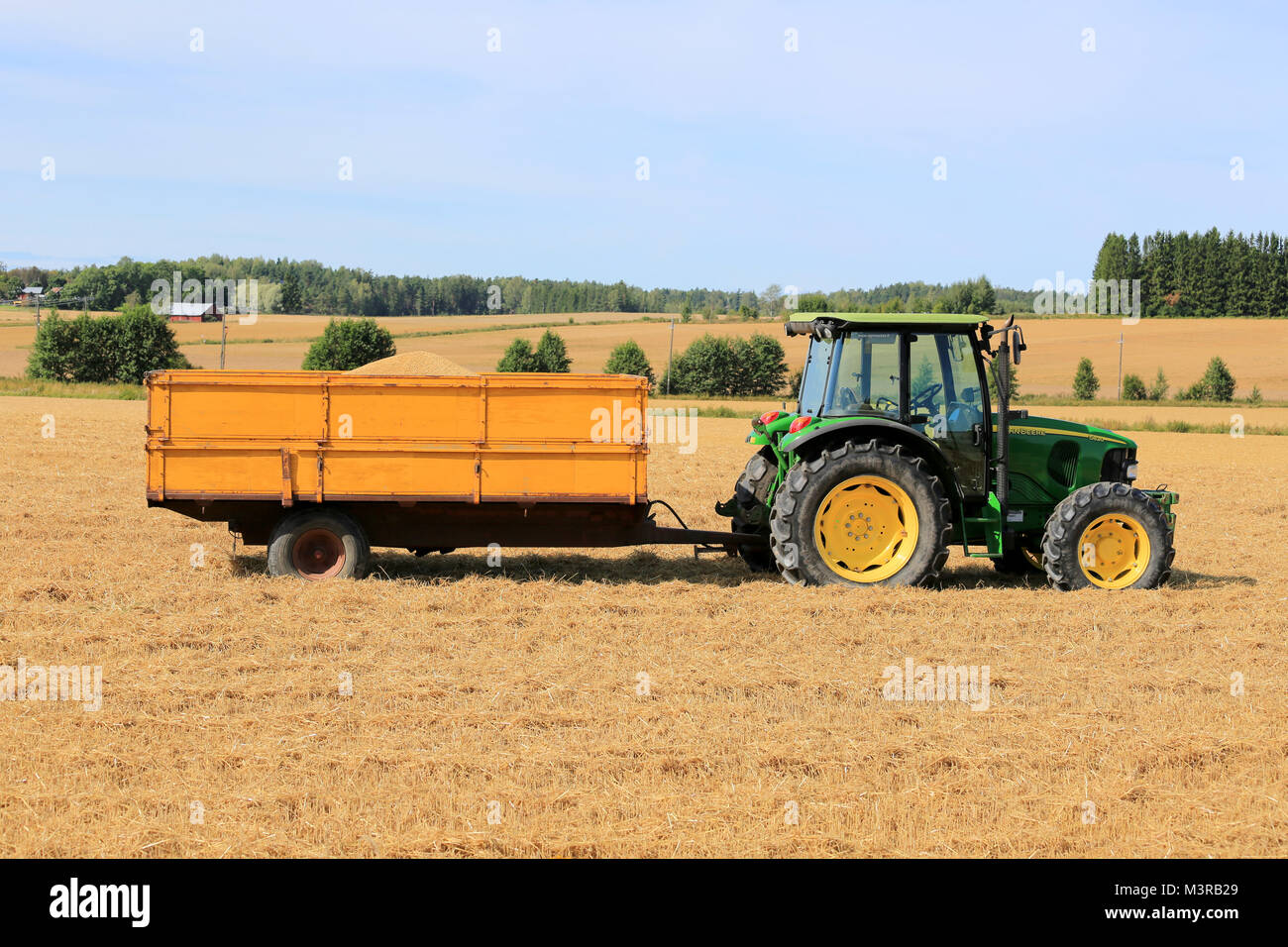 RAASEPORI, Finnland - 17. AUGUST 2014: John Deere 5820 Traktoren und Anhänger voller Korn auf Stoppeln Feld. John Deere 5820 wurde herstellen Stockfoto