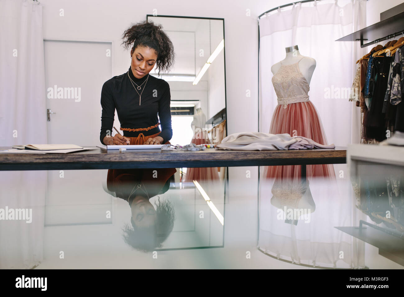 Weibliche Mode Designer entwerfen ein Design an Ihrem Tisch sitzen. Modeunternehmer vertieft in eine Zeichnung an Ihrem Schreibtisch in ihrem Tuch Shop. Stockfoto
