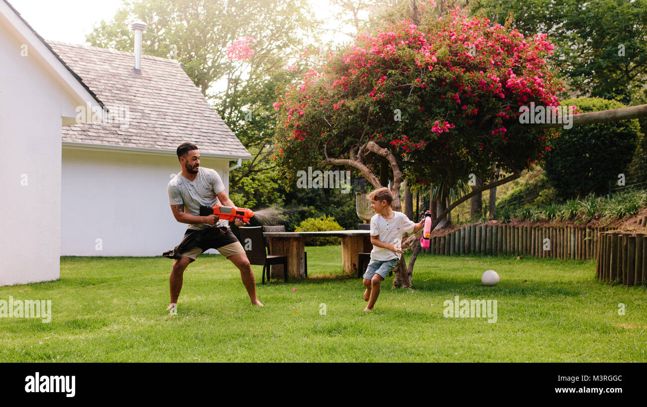 Mann spielt mit kleinen Jungen im Hinterhof rasen. Vater und Sohn spielen mit Wasserkanonen im Freien. Stockfoto