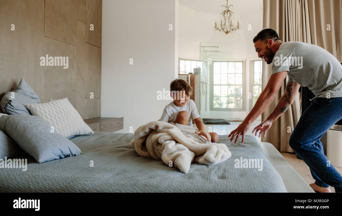 Vater und Sohn spielen im Schlafzimmer. Verspielt Vater über seinen kleinen Sohn auf dem Bett zu sitzen, zu Hause zu holen. Stockfoto