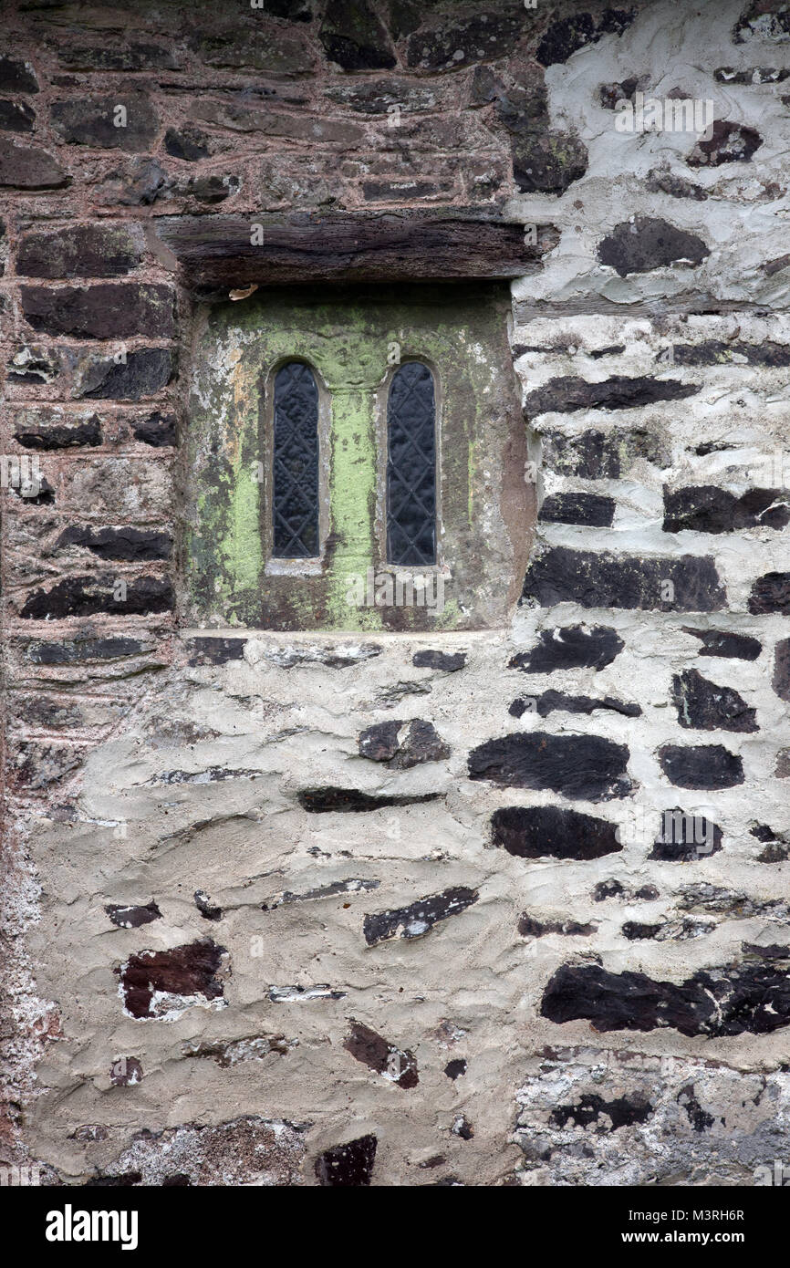 Sächsische Fenster mit einem Gesicht, Teil-Cat, Teil-Mann, der sich oben auf der Säule zwischen den beiden Fenster leuchten, St Beuno's Kirche, Culbone in Somerset, England. Stockfoto