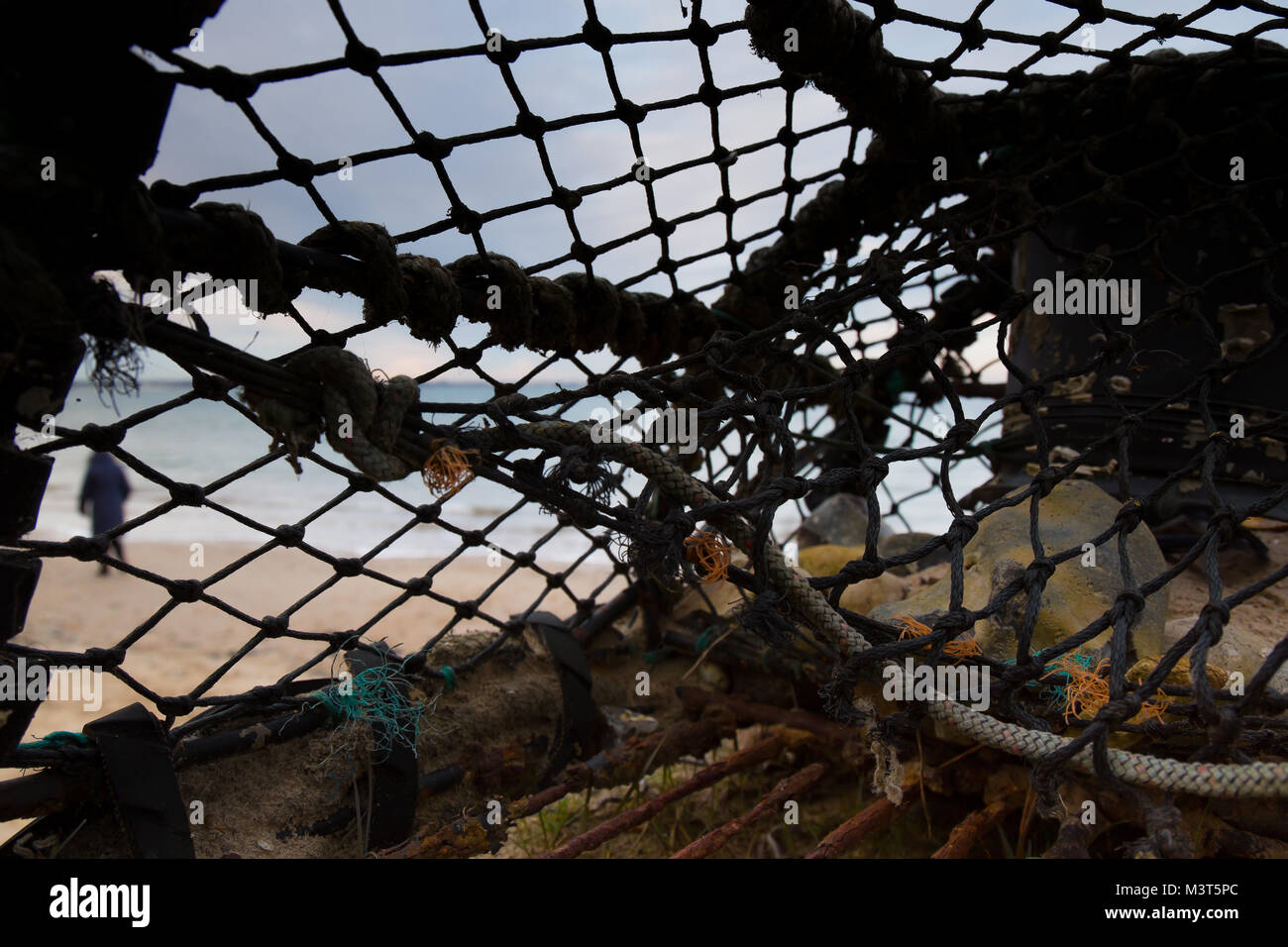 In der Nähe von alten, ausrangierten Lobster Pot am Strand verlassen, unter den Trümmerteilen gewaschen an Land durch die Gezeiten. Weichzeichner Strand bei Sonnenuntergang, durch Netting sichtbar. Stockfoto