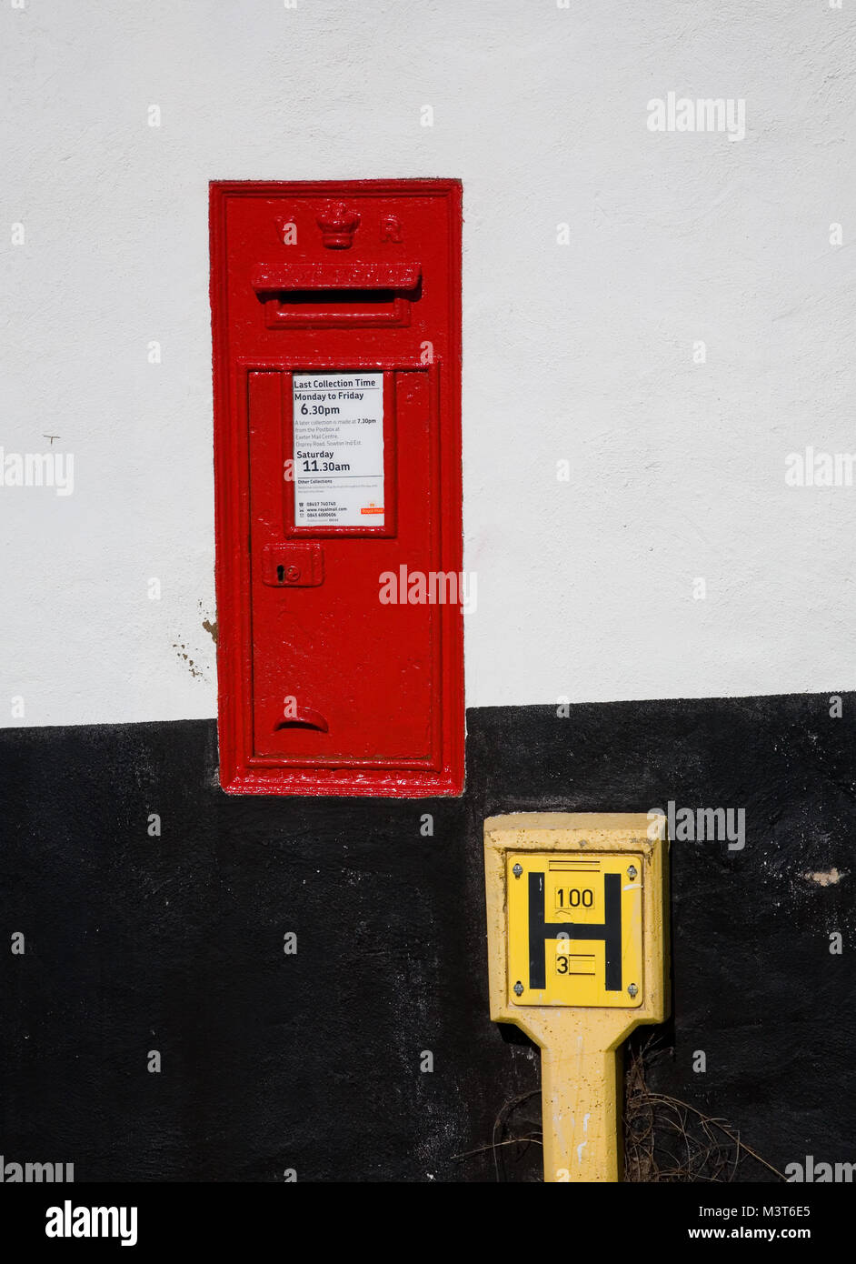 Red Victorian postbox und gelben Hydranten Marker schwarz und weiß gestrichenen Wand, Bath, Devon, Großbritannien. Stockfoto