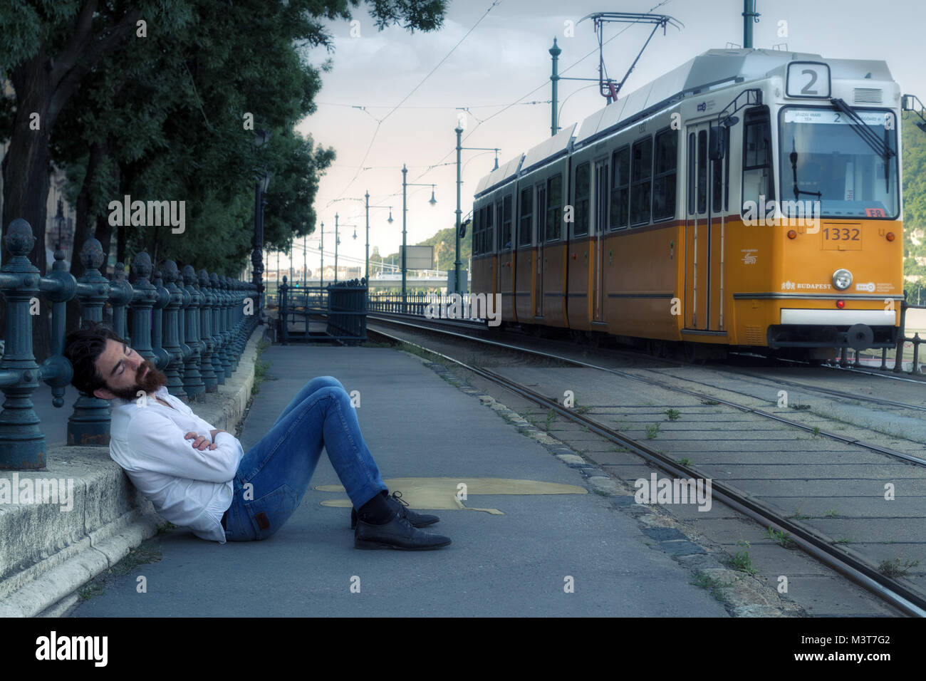 Junger Mann schläft auf dem Boden an der Straßenbahnhaltestelle Stockfoto