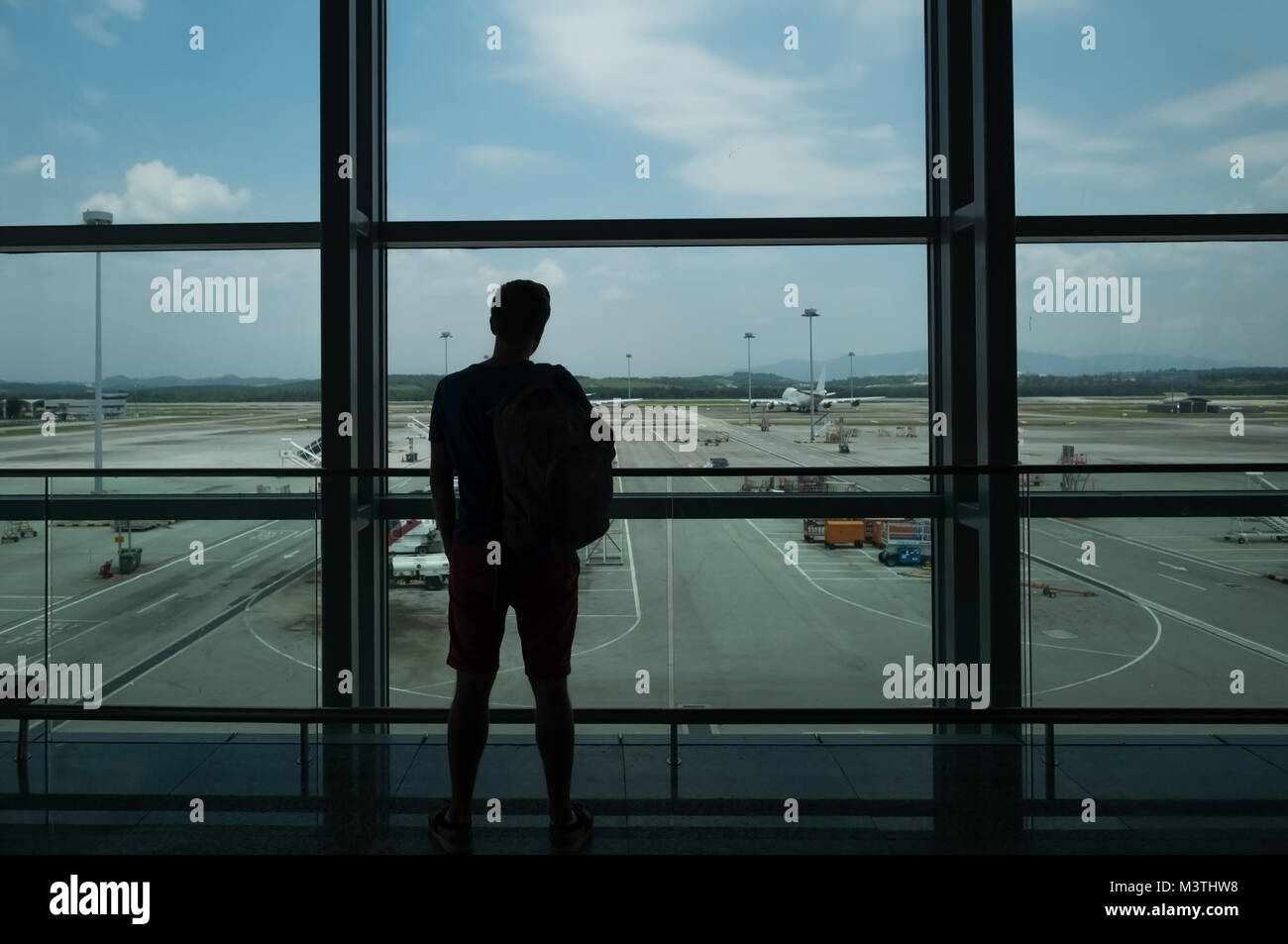 Junge Mann steht in der Nähe der Fenster am Flughafen und Flugzeug vor dem Abflug. Stockfoto