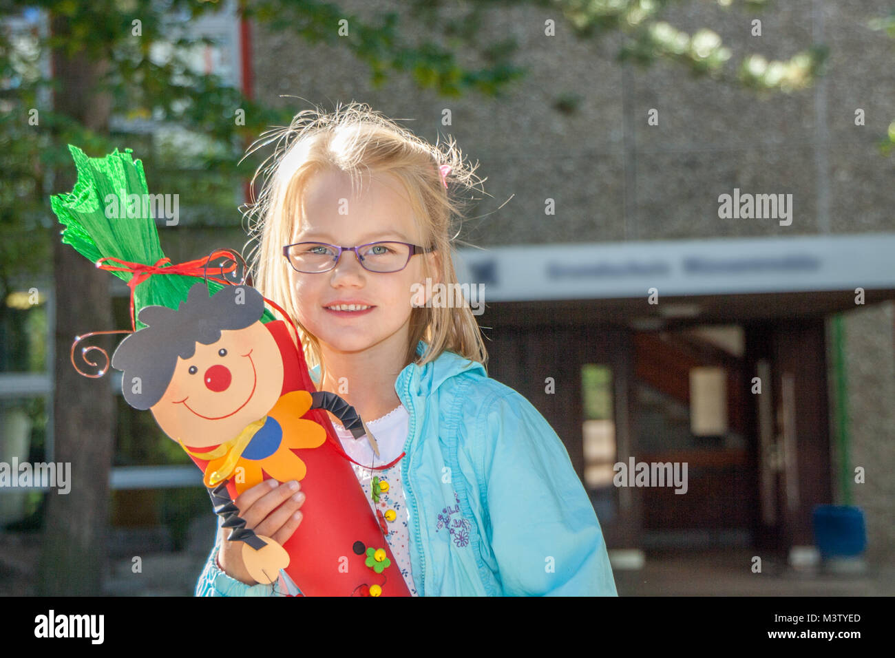 Portrait von stehendes Mädchen vor der Schule Eingang und freuen uns auf Ihren ersten Tag in der Schule mit einer Süßigkeit Kegel in Ihrer Hand Stockfoto