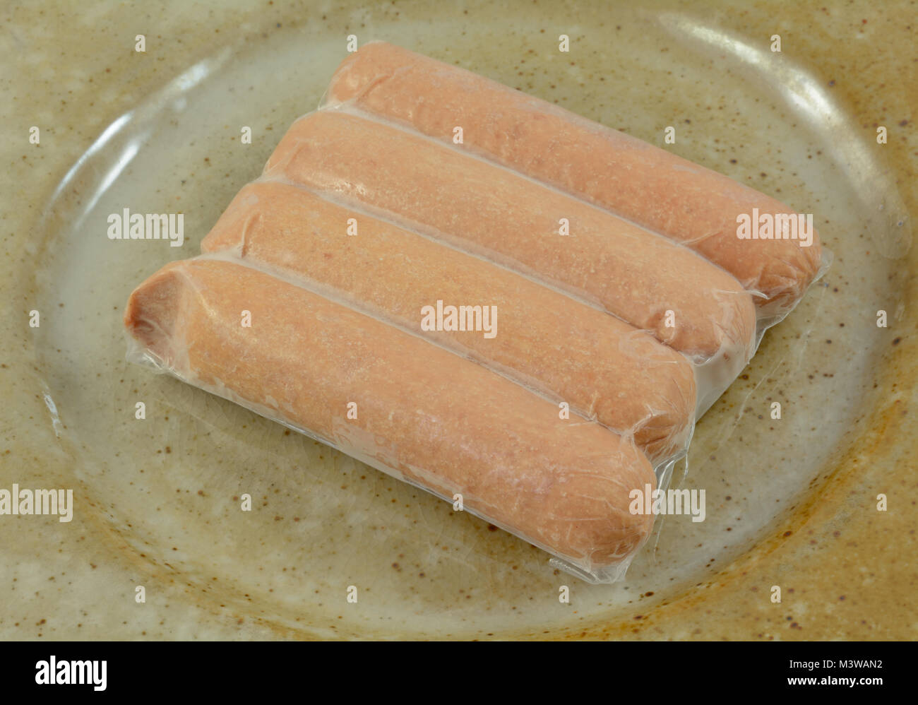 Gefrorenes Schweinefleisch und Rindfleisch Hot Dogs in Kunststoff Verpackung Auftauen auf Keramikplatte Stockfoto