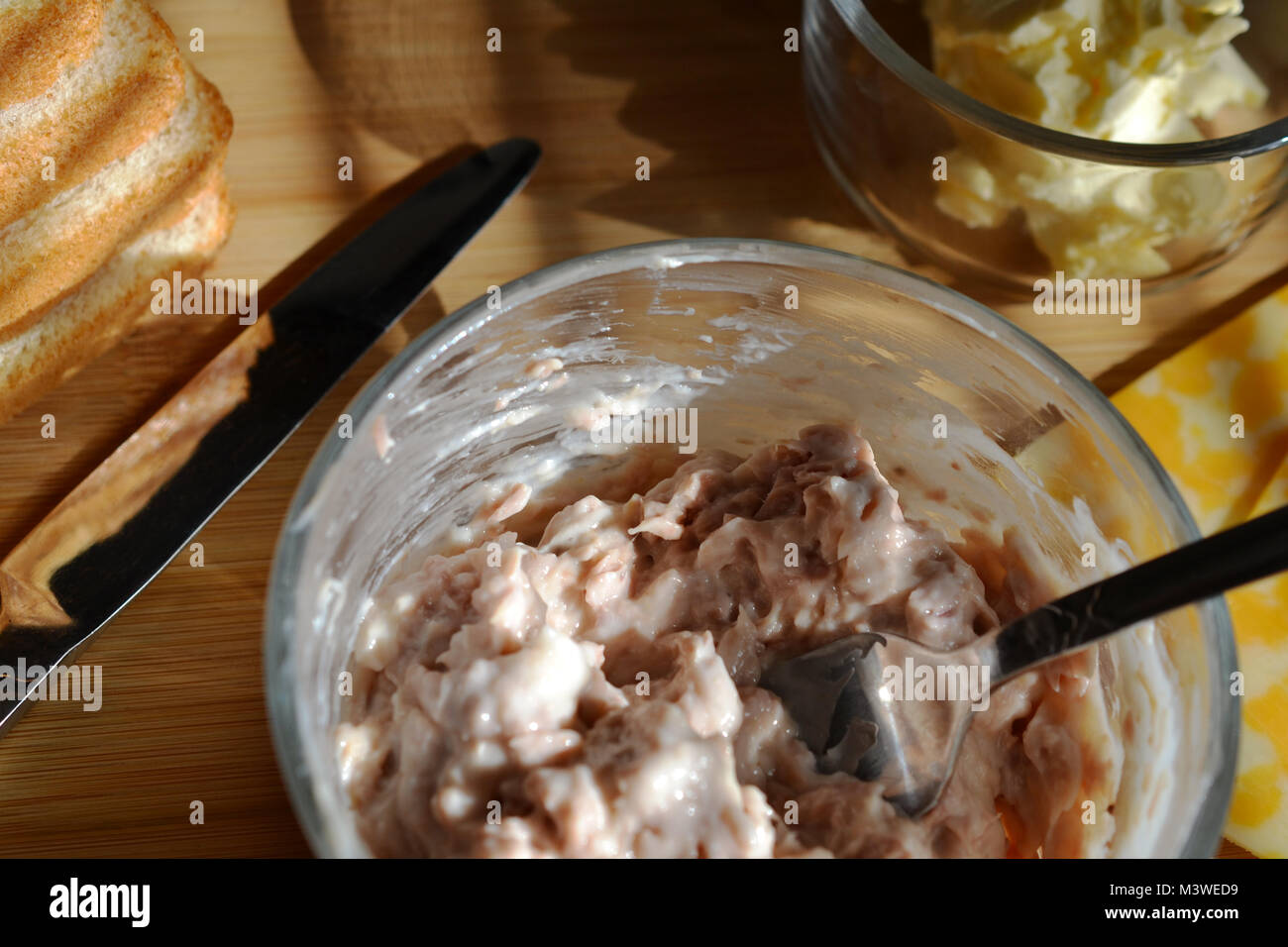 Thunfisch Salat im Glas Schüssel mit Silber Gabel in der Schüssel, Holz Hintergrund, Schlagsahne Butter in Glashalter, Butter Messer, n Toast Stockfoto