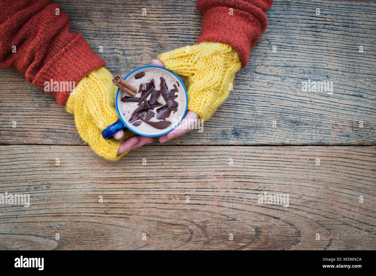 Womans Hände mit gelben woollen Handschuhe halten einer Tasse heißer Schokolade mit einer Zimtstange und dunkler Schokolade Spänen von oben Stockfoto