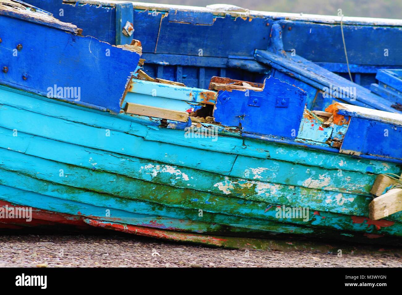 Völlig ruiniert und Holzboot mit hellen blauen Lackierung aufgegeben am Strand links oben zu brechen. Stockfoto