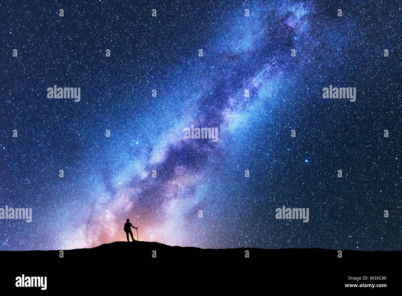 Silhouette der Mann mit Trekking Polen gegen die unglaubliche Milchstraße in der Nacht. Raum Hintergrund. Landschaft mit Mann auf dem Hügel, hellen Milchstrasse, Himmel mit Stockfoto