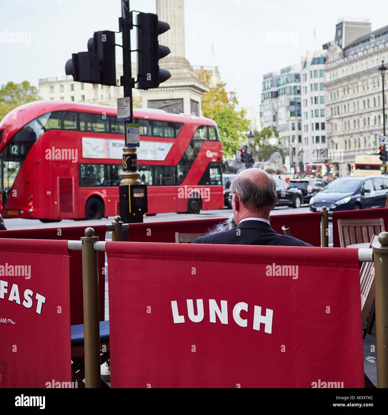 Rückansicht des sitzenden Menschen rauchen allein außerhalb von London Restaurant mit London Bus im Hintergrund Stockfoto