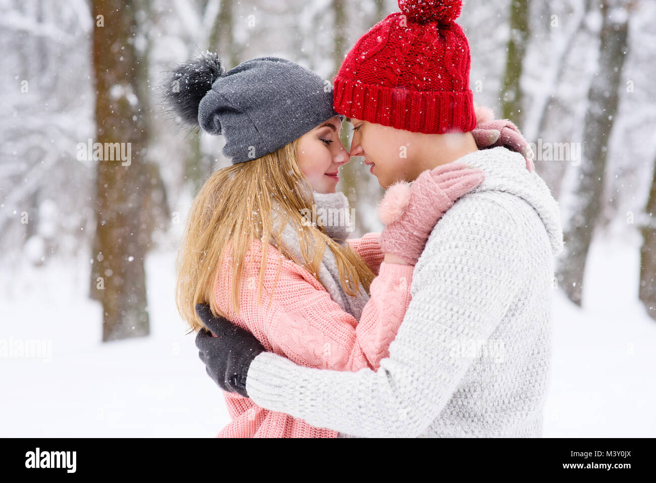 Portrait von gilr und junge halten einander auf gestrickte Pullover und Mützen bei Schneefall Stockfoto