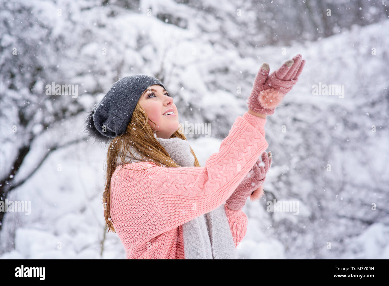 Junge glücklich Frau in rosa Pullover, Handschuhe, Schal und Mütze bei Schneefall Stockfoto